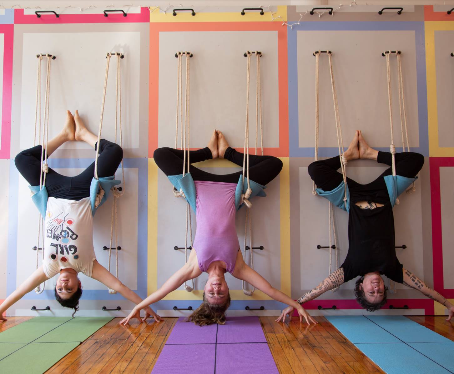 Three women hanging upside down in the Samamkaya Yoga Collective studio.