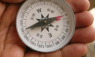 Hand holding a compass with needle aligned North and South.