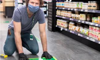 co-op employee placing social distancing graphic on the floor of a grocery aisle.