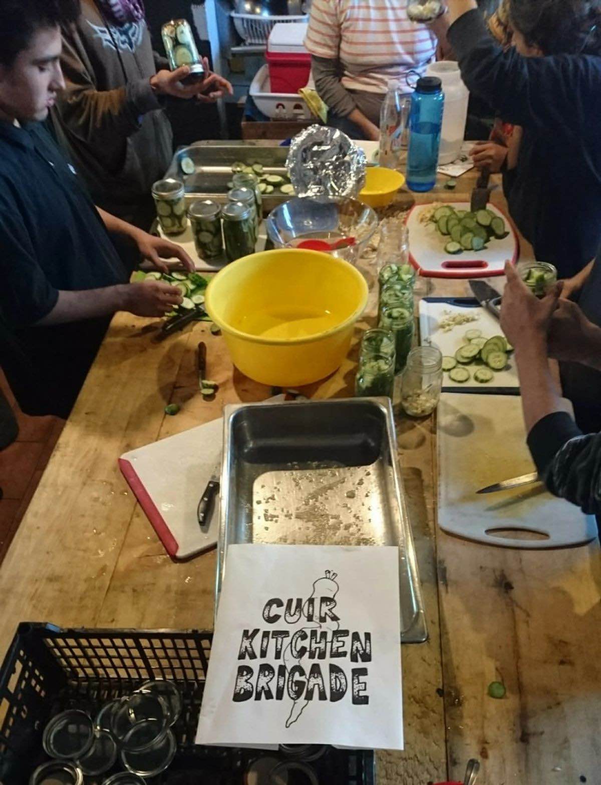 Volunteers making cucumber pickles on a long wooden table.