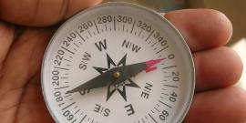 Hand holding a compass with needle aligned North and South.